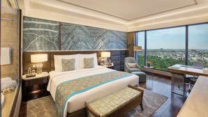 A modern hotel room with a large bed, a desk, and a view of the city.