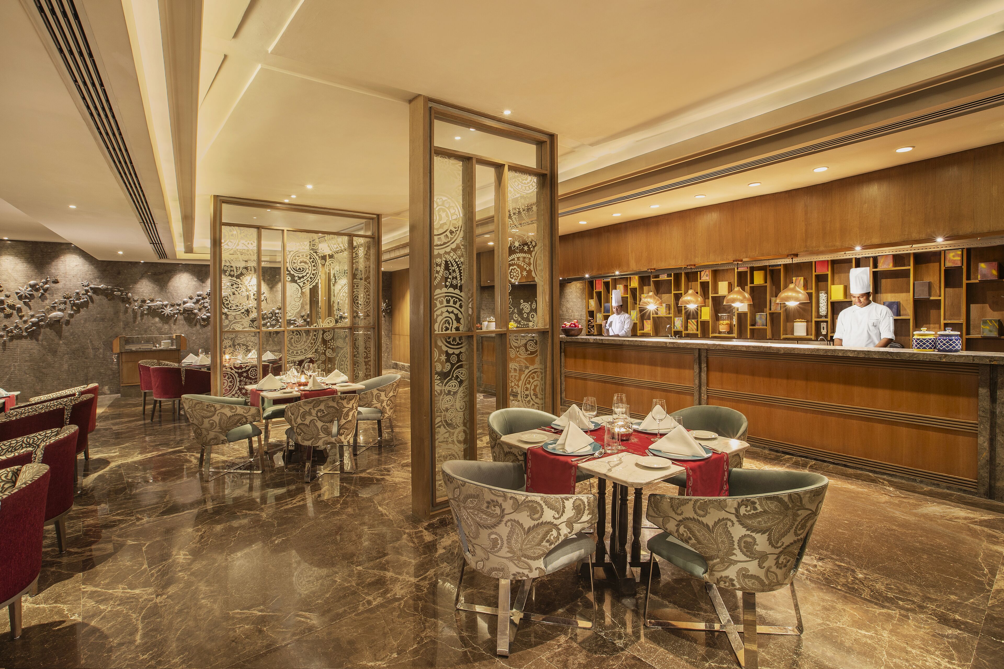 Um restaurante com piso de mármore, cadeiras estampadas e um bar com um chef.