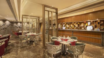 Um restaurante com piso de mármore, cadeiras estampadas e um bar com um chef.