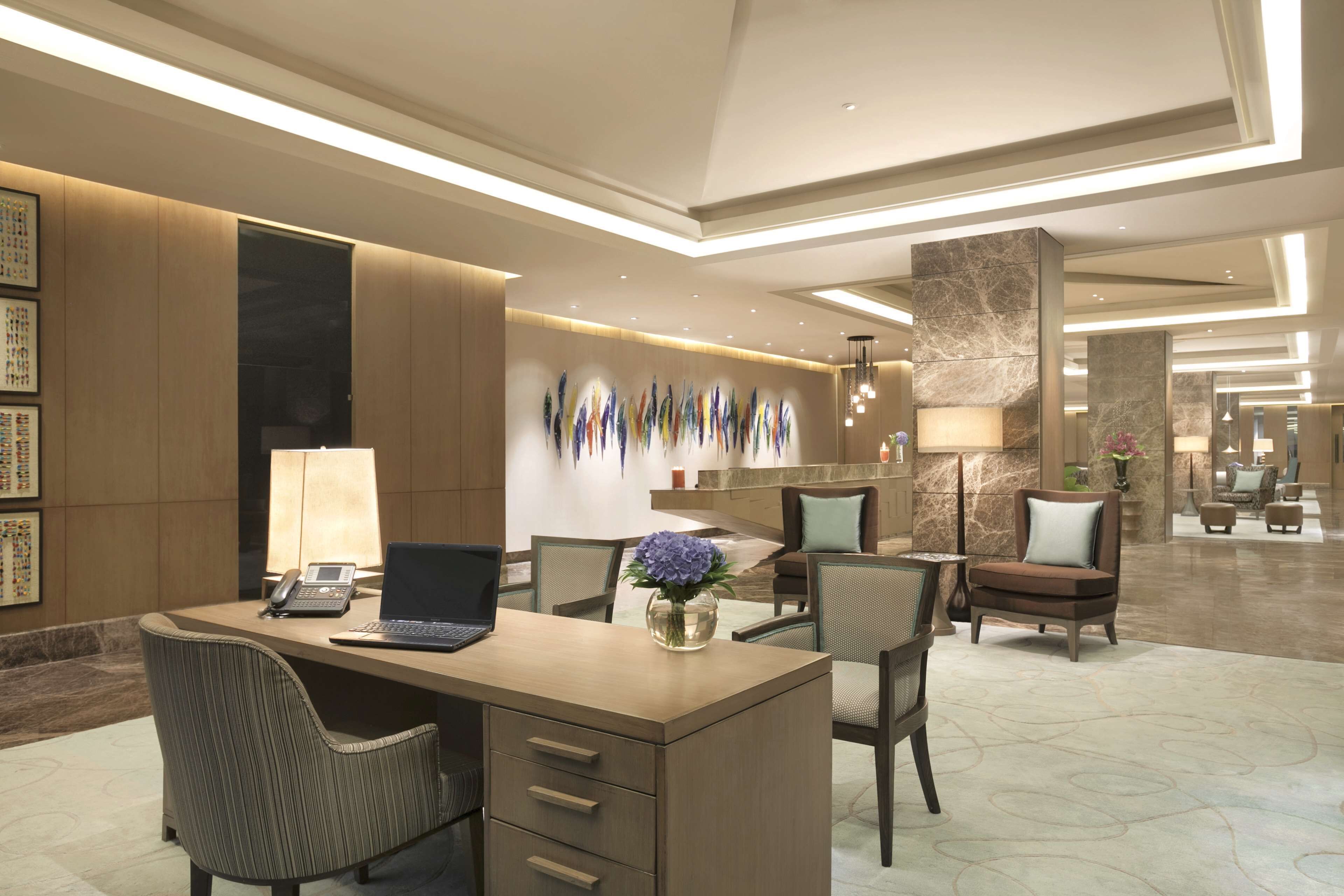 A modern hotel lobby with a reception desk, seating area, and decorative wall art.