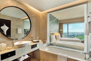 A modern bathroom with a large oval sink, a mirror, a bathtub, and a large window offering a city view.
