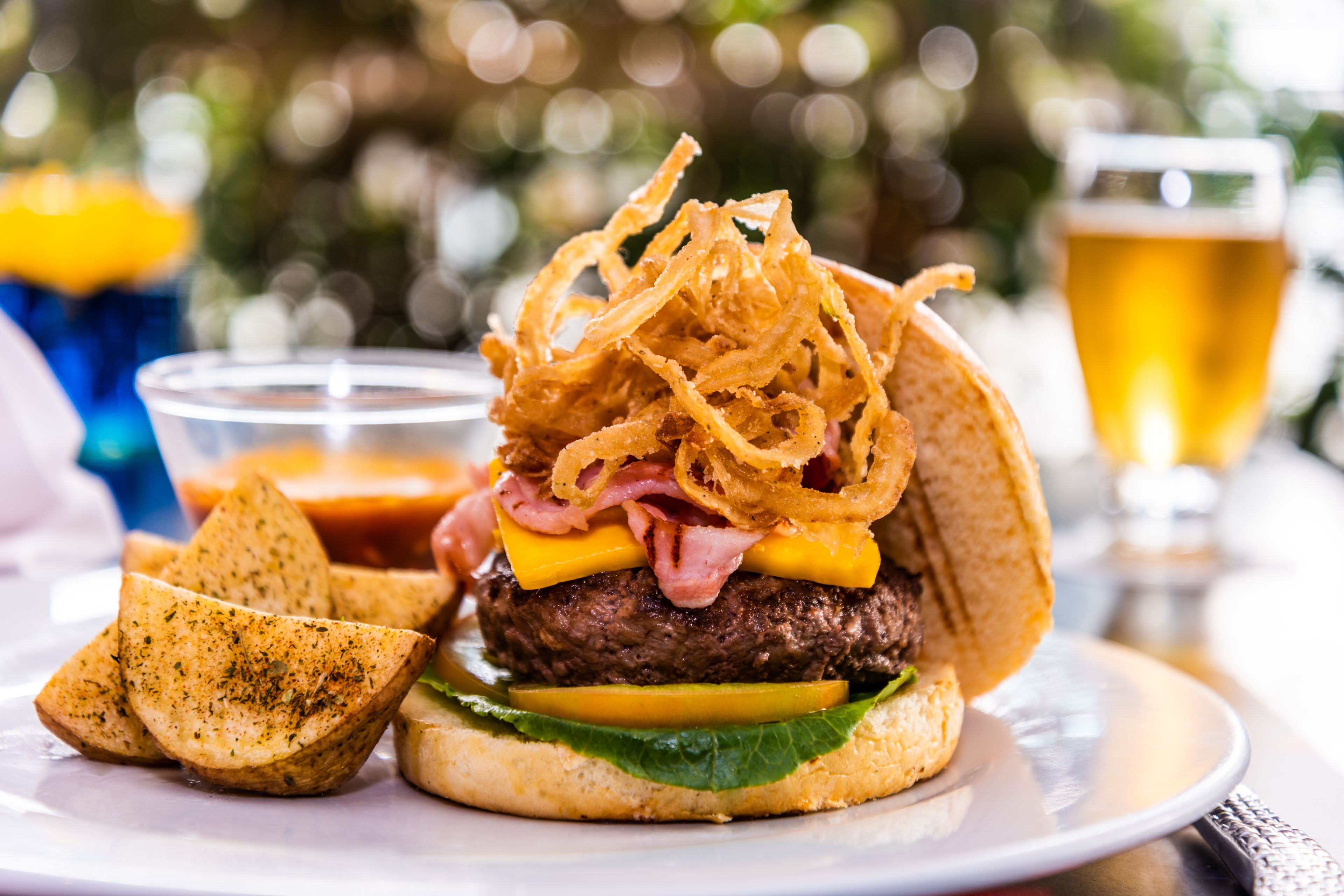 Ein Burger mit Speck, Käse und Salat auf einem Brötchen, dazu Zwiebelringe und ein Glas Bier.