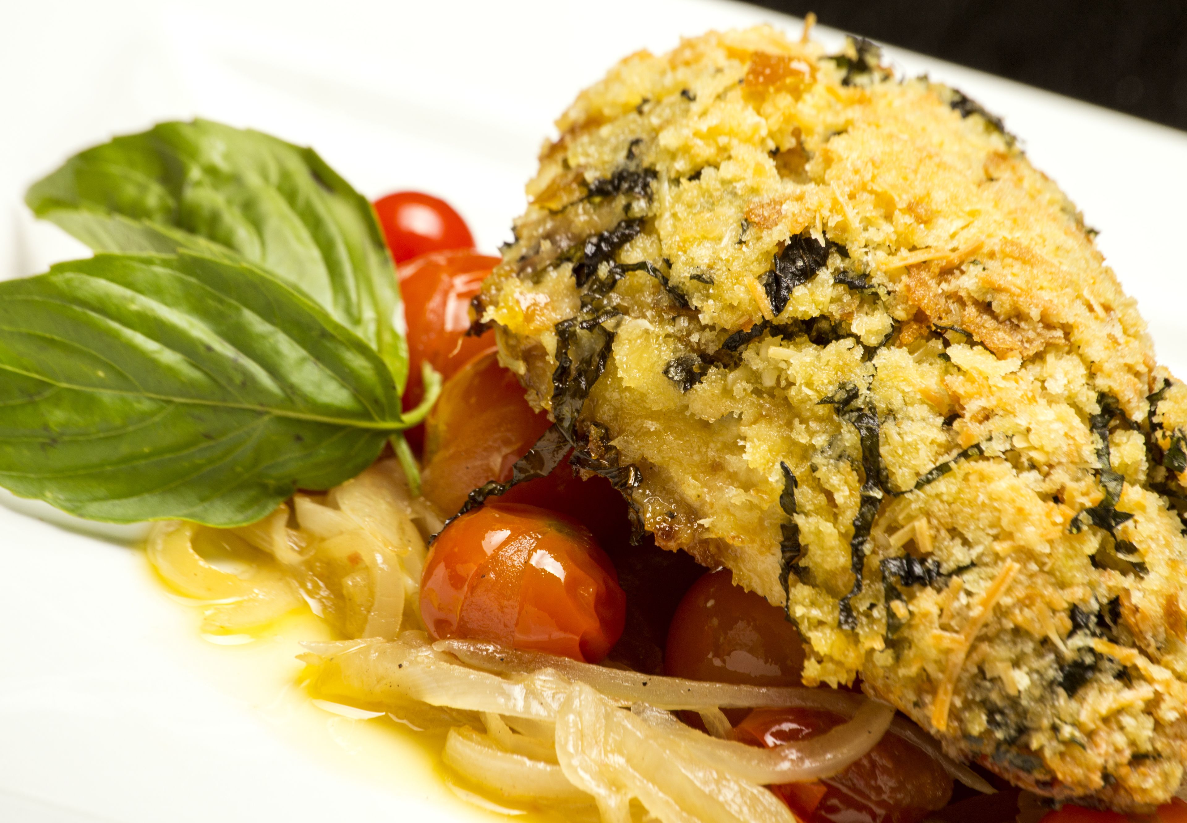 A dish with a breaded item, cherry tomatoes, and basil on a white plate.