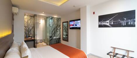 A modern hotel room with a bed, a TV, a painting, and a wooden bench.