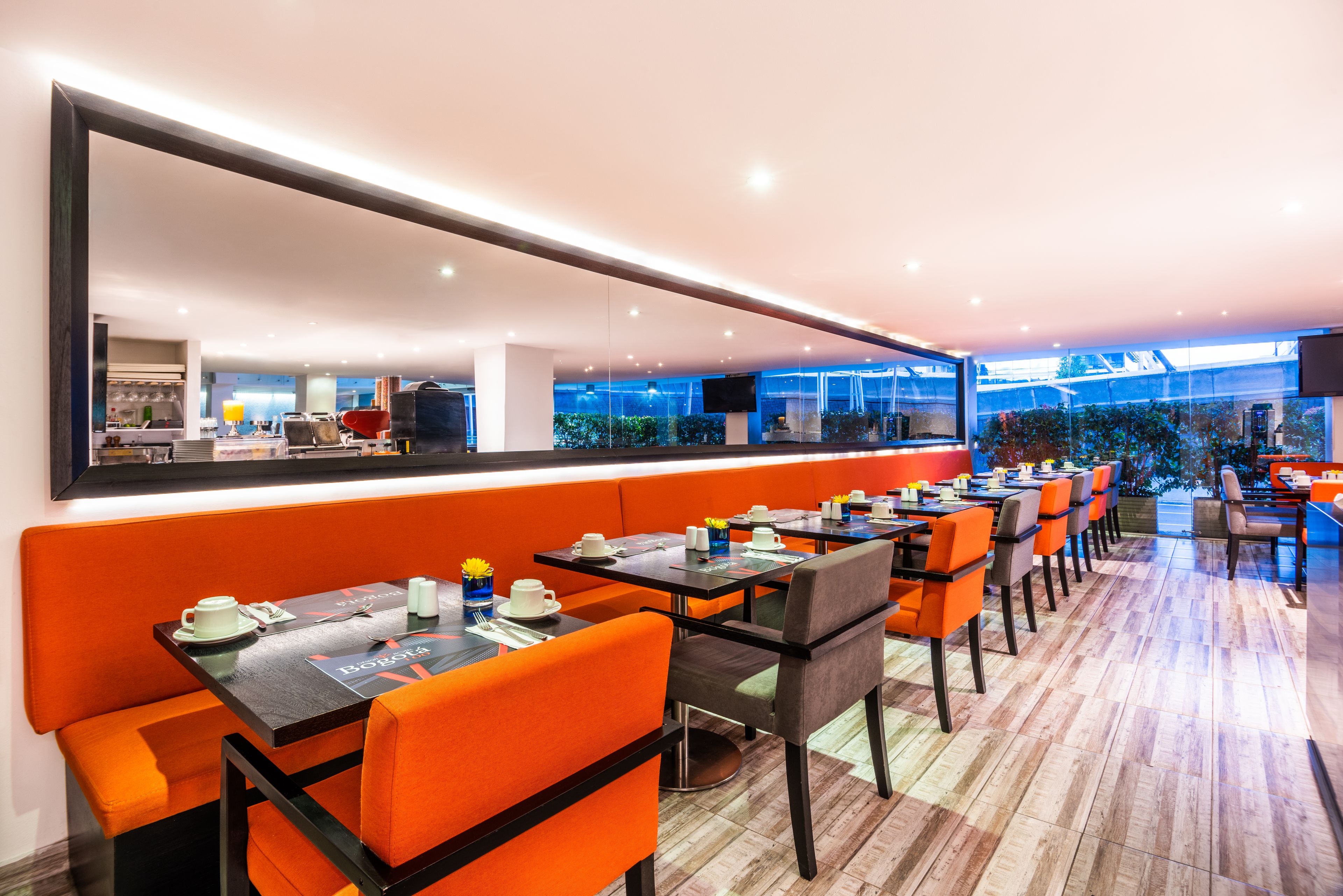 A modern restaurant with orange seating, a large mirror, and a view of the outdoor area.
