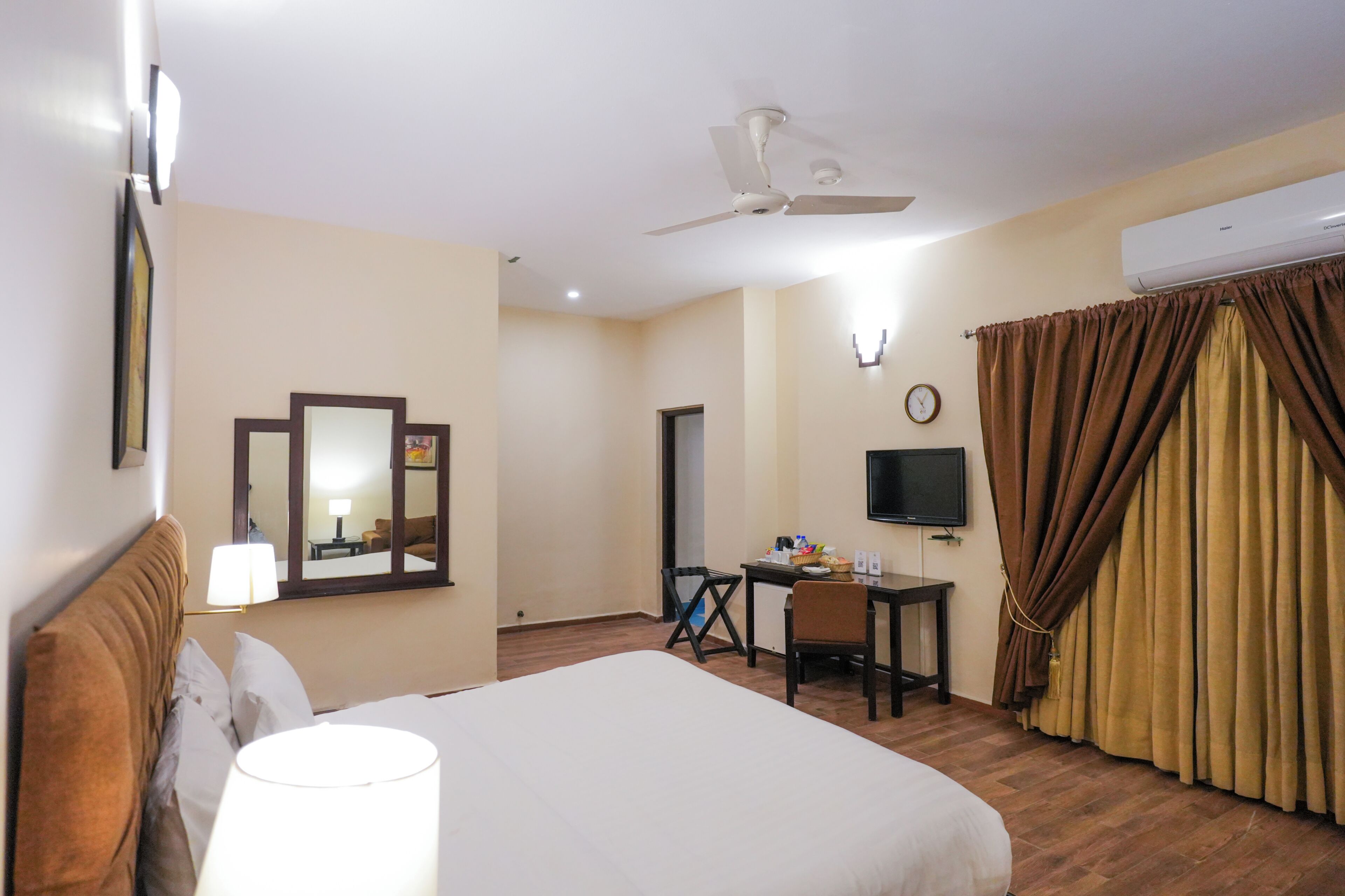 Une chambre d’hôtel équipée d’un lit, d’un bureau, d’une chaise, d’une télévision, d’un ventilateur de plafond et d’un appareil de climatisation.