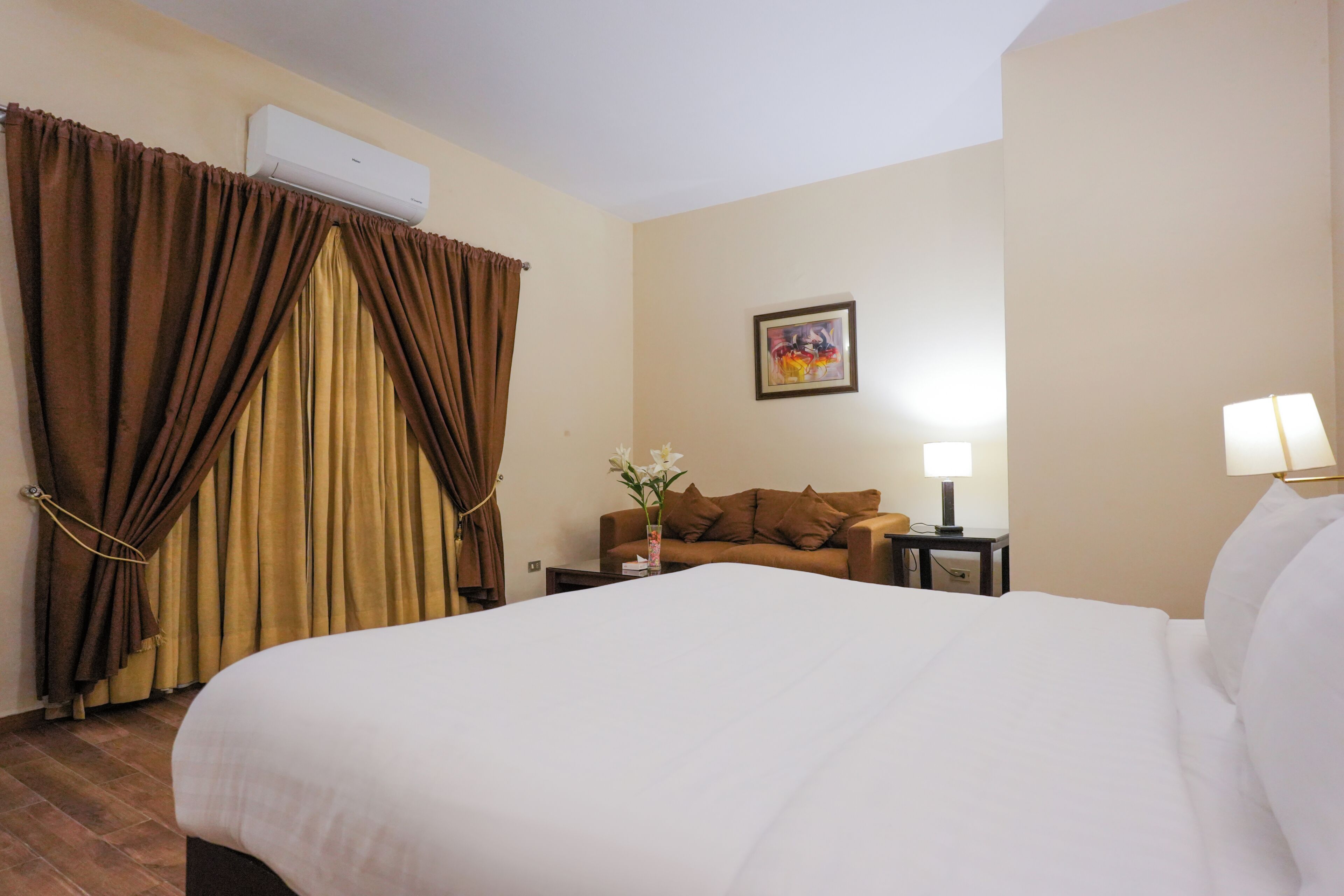 Une chambre d’hôtel avec un grand lit, un canapé, une table de chevet avec une lampe et un appareil de climatisation.