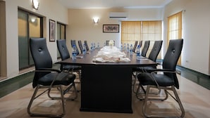 Uma sala de conferências com uma mesa comprida, cadeiras pretas, garrafas de água e toalha de mesa branca.