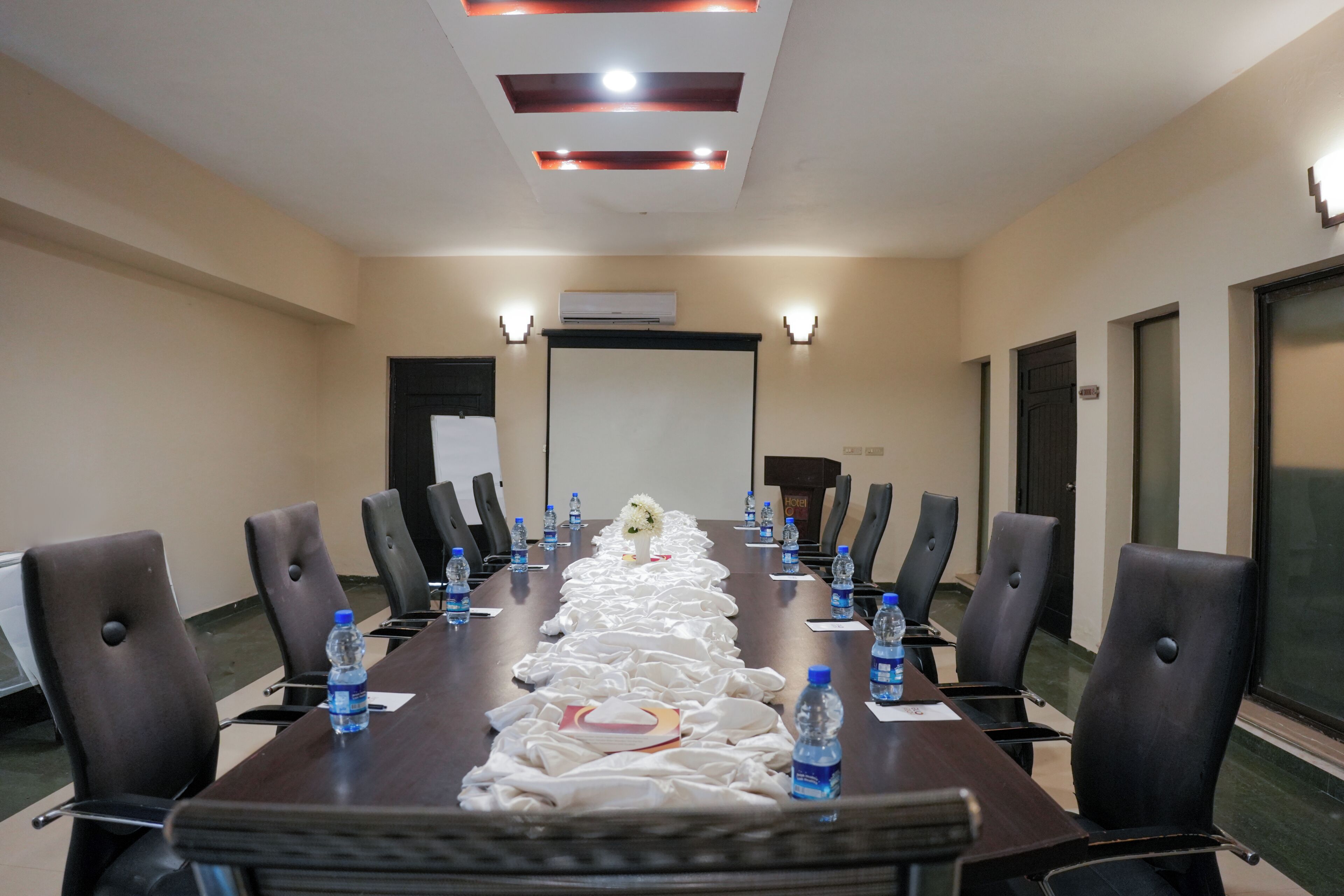 A conference room with a long table, chairs, water bottles, and a projector screen.