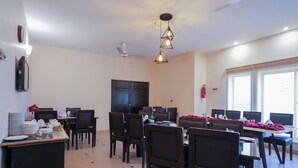 Uma área de refeições com várias mesas e cadeiras, um ventilador de teto e um extintor de incêndio.