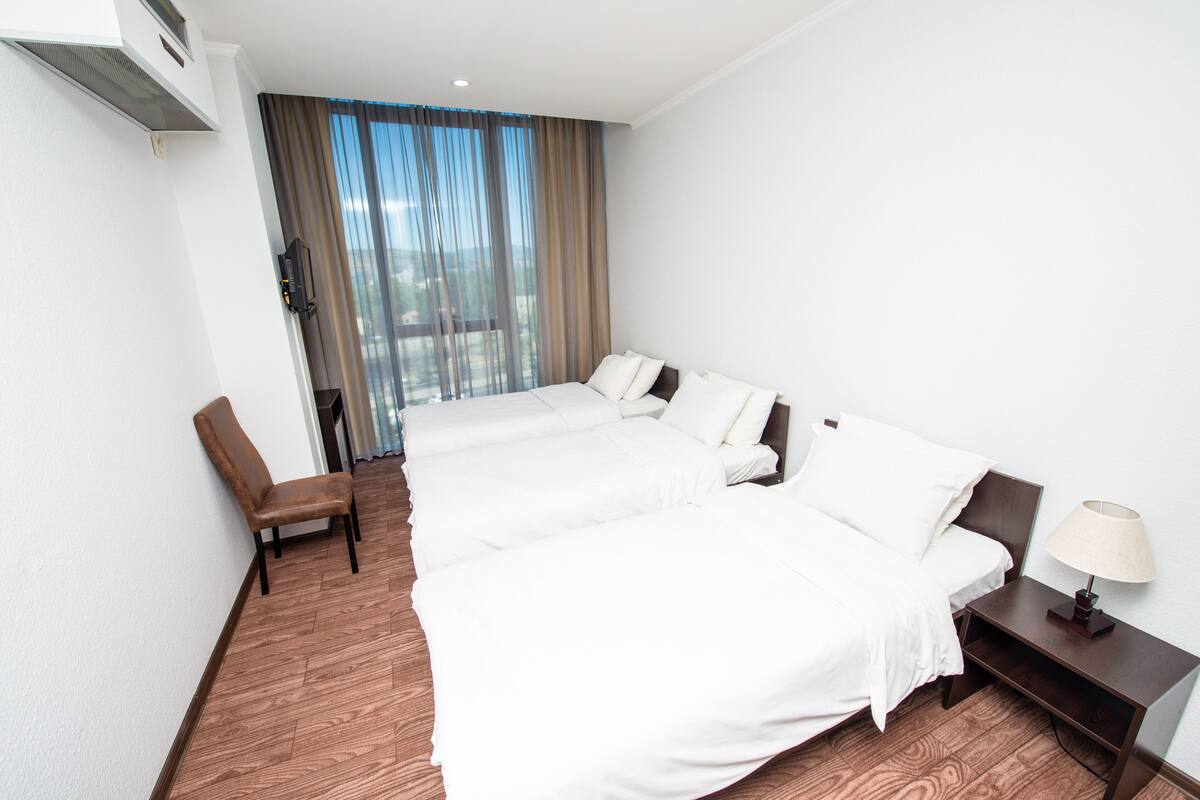 Habitación de hotel con una cama grande, una silla, una mesita de noche y una ventana con cortinas.
