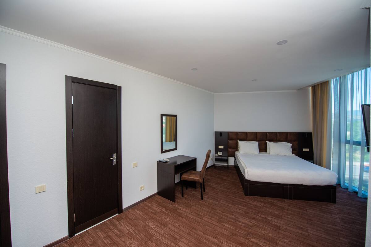 Habitación de hotel con una cama grande, un escritorio, una silla, un armario y una ventana con cortinas.