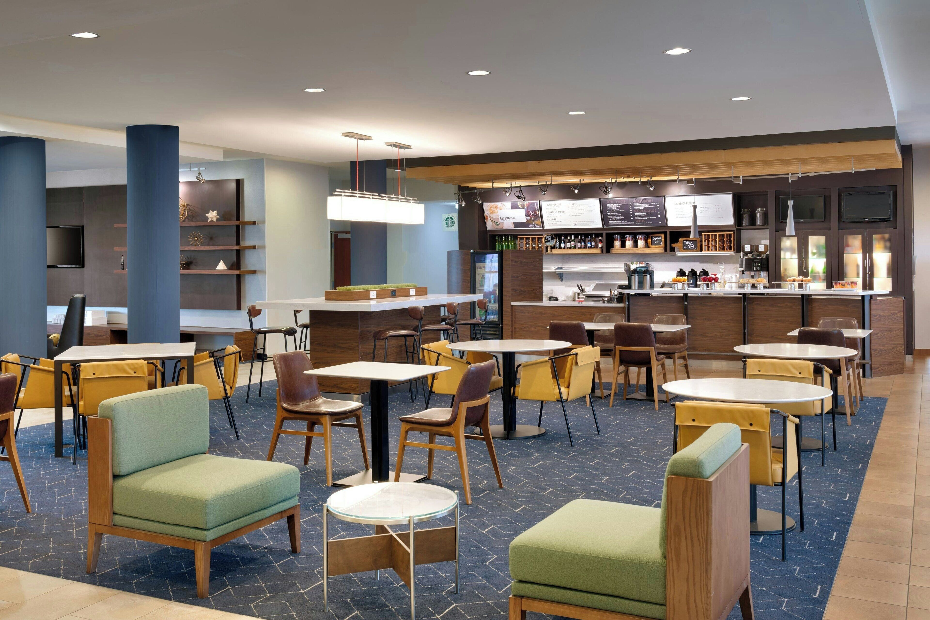 A modern restaurant with multiple seating areas, including tables and chairs, and a bar counter with various food and drink items.