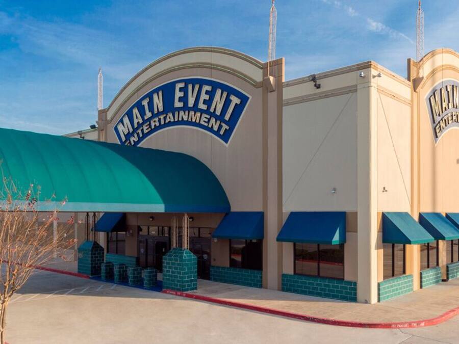 A Main Event Entertainment building with a large sign, covered entrance, and blue awnings.