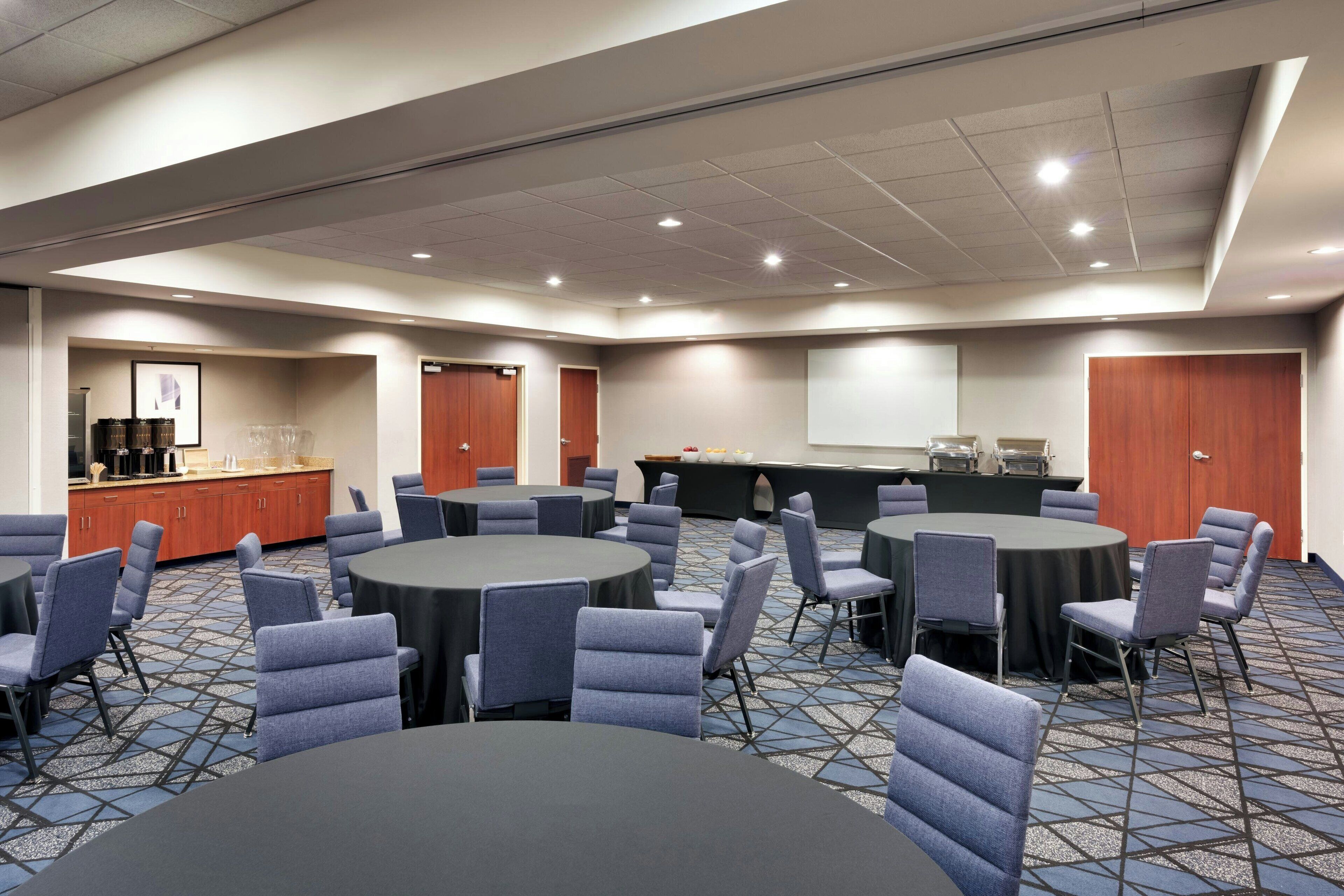 A conference room with round tables and chairs, a coffee station, and a projection screen.