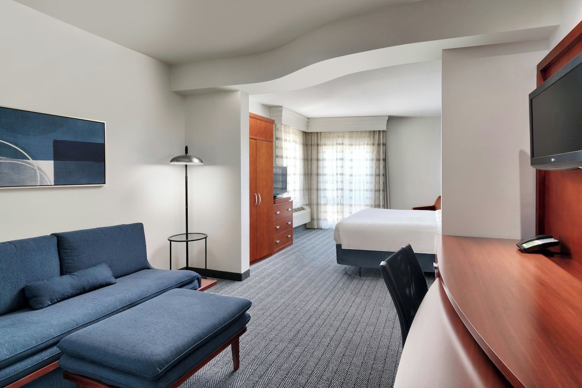 Une chambre d’hôtel équipée d’un canapé, d’un lit, d’un bureau, d’une télévision, d’une armoire et d’un tableau au mur.