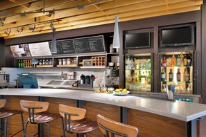 A modern bar area with a long counter, bar stools, a menu board, and a refrigerator stocked with bottles. - Courtyard by Marriott Houston NASA/Clear Lake (Houston)