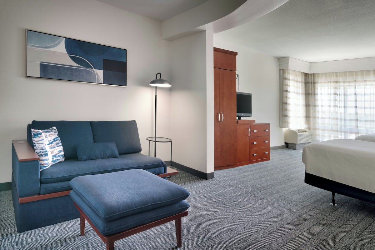 Une chambre d’hôtel équipée d’un canapé, d’un pouf, d’une télévision à écran plat, d’une armoire et d’un lit.
