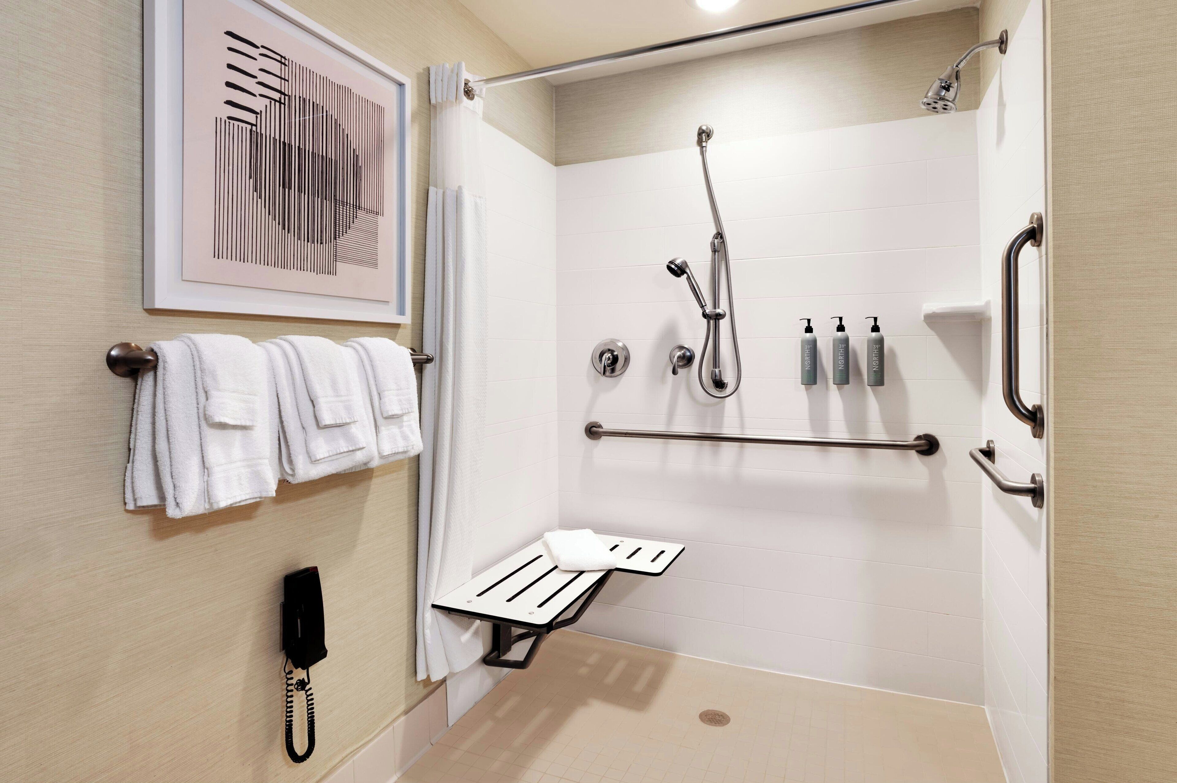 A modern bathroom with a shower, grab bars, a towel rack, and a phone.