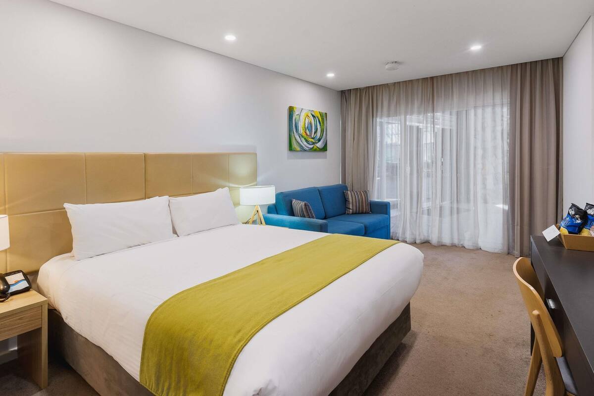 Una camera d'albergo con un letto, un divano blu, una scrivania e un quadro appeso al muro.