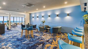 A modern hotel lobby with a blue carpet, seating area, and a view of the ocean.