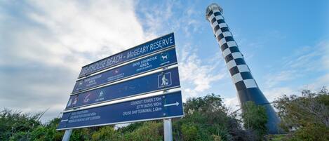 A directional sign with multiple destinations including a lighthouse, dog exercise area, public toilets, and a lookout tower.