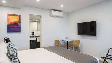Quarto de hotel com cama, escrivaninha, cadeira, televisão, ar condicionado e um quadro na parede.