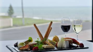 A table with a charcuterie board, two glasses of wine, and a view of the ocean.