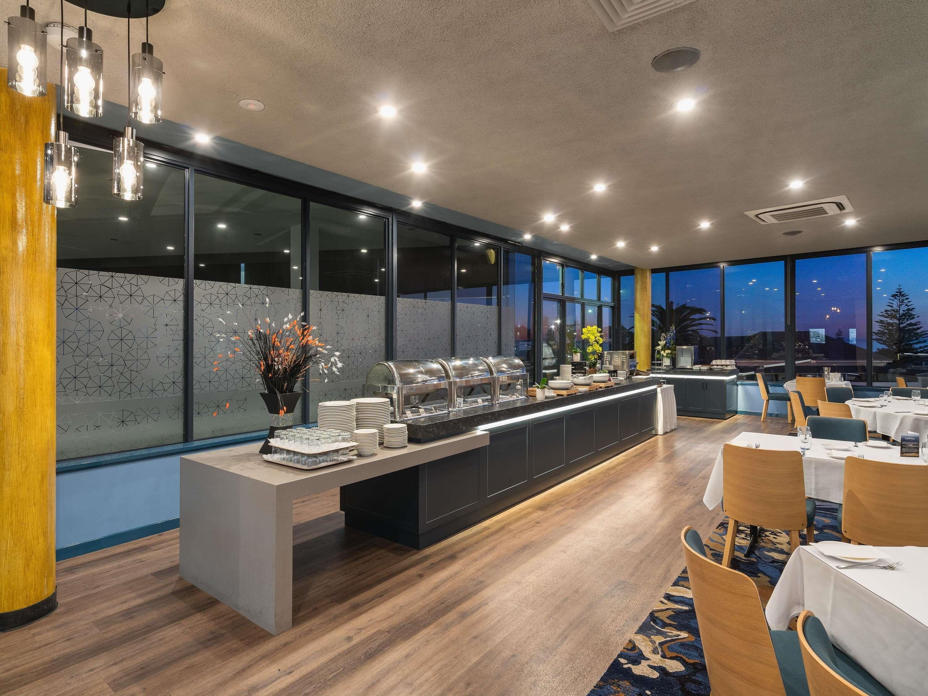 Un restaurant moderne doté d’un buffet, de grandes fenêtres et offrant une vue sur le paysage urbain au crépuscule.
