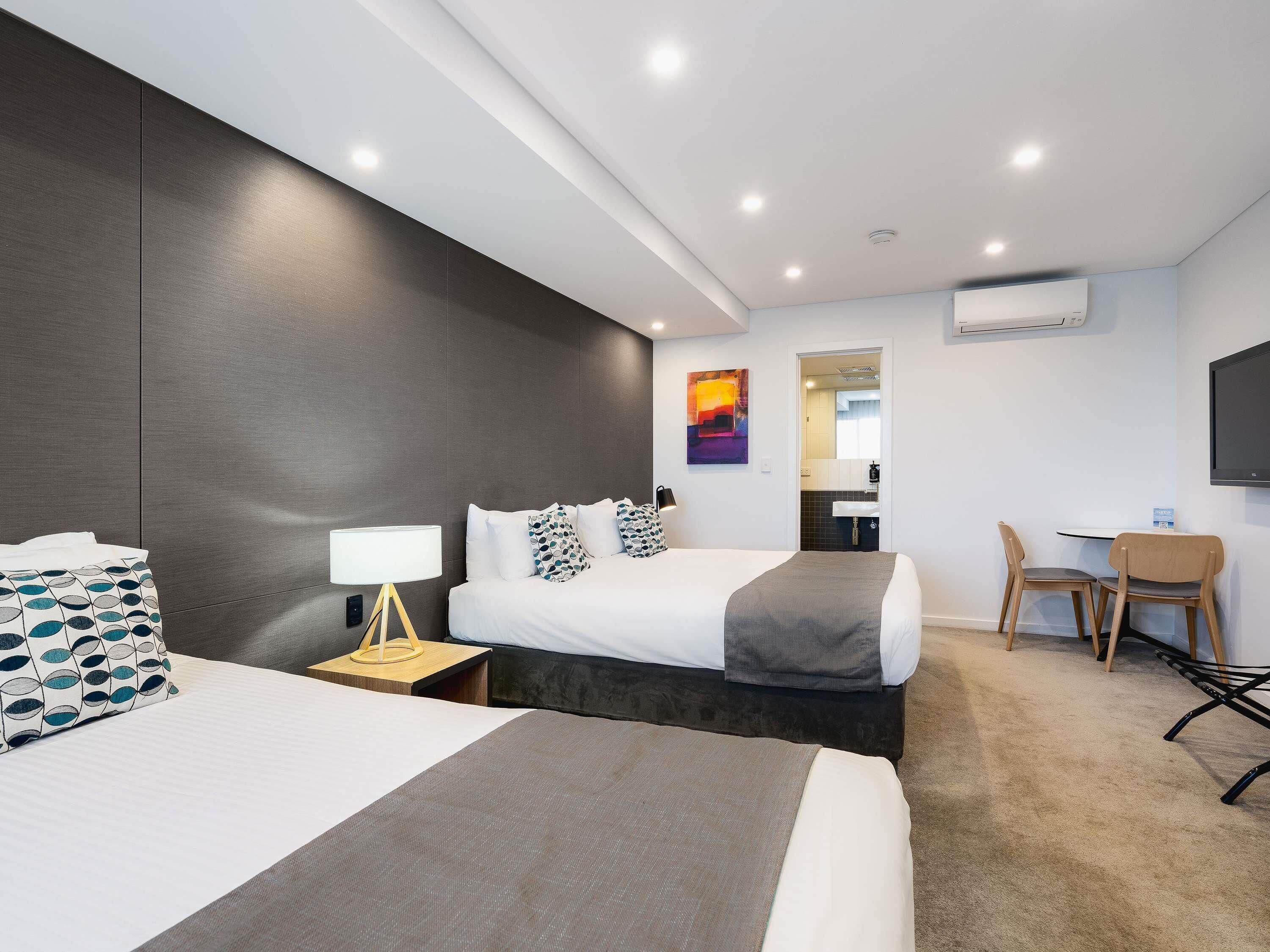 A modern hotel room with two beds, a desk, a chair, and a TV.