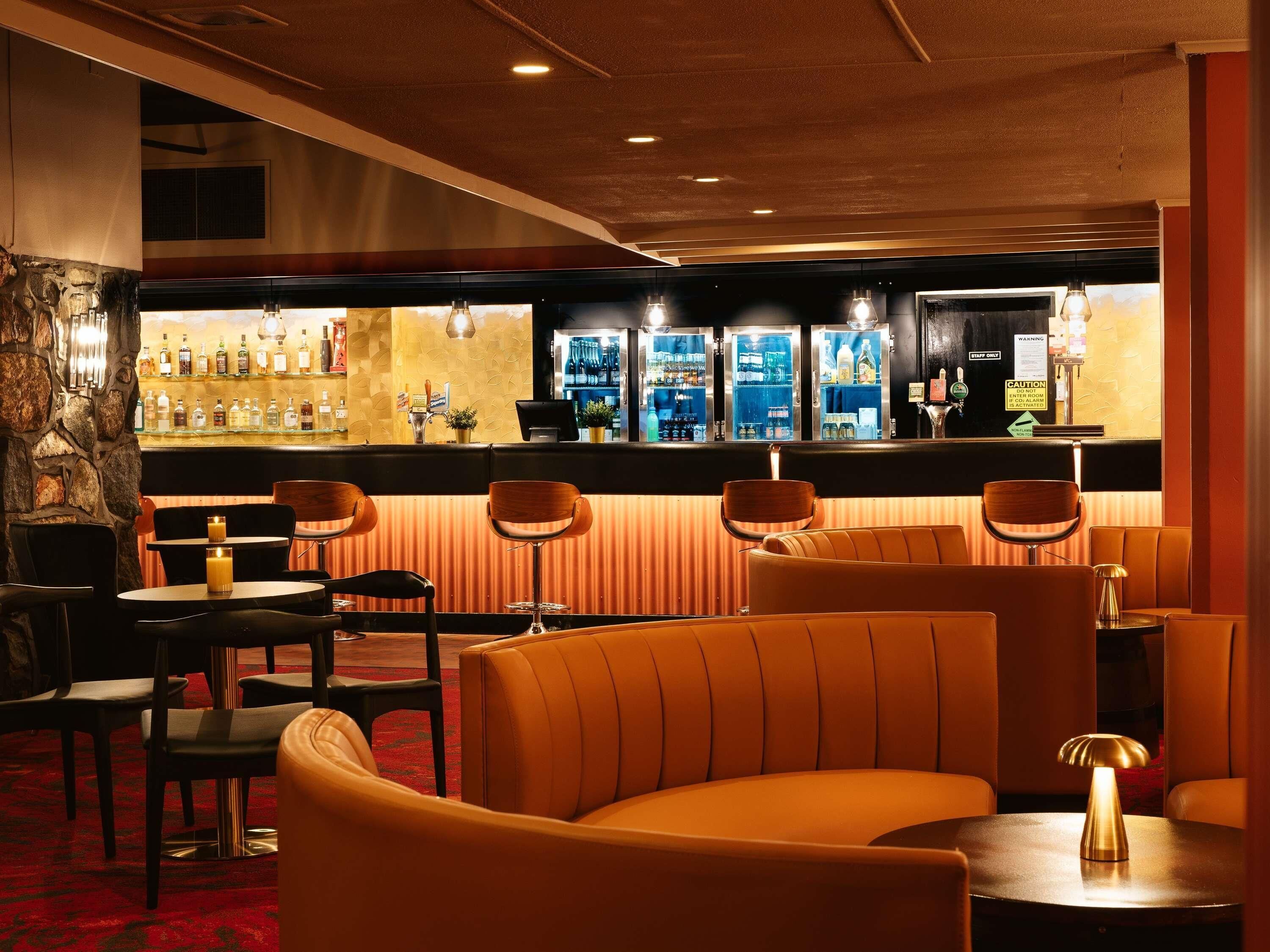 Een bar met zitplaatsen, een stenen muur en een toonbank met verschillende flessen.