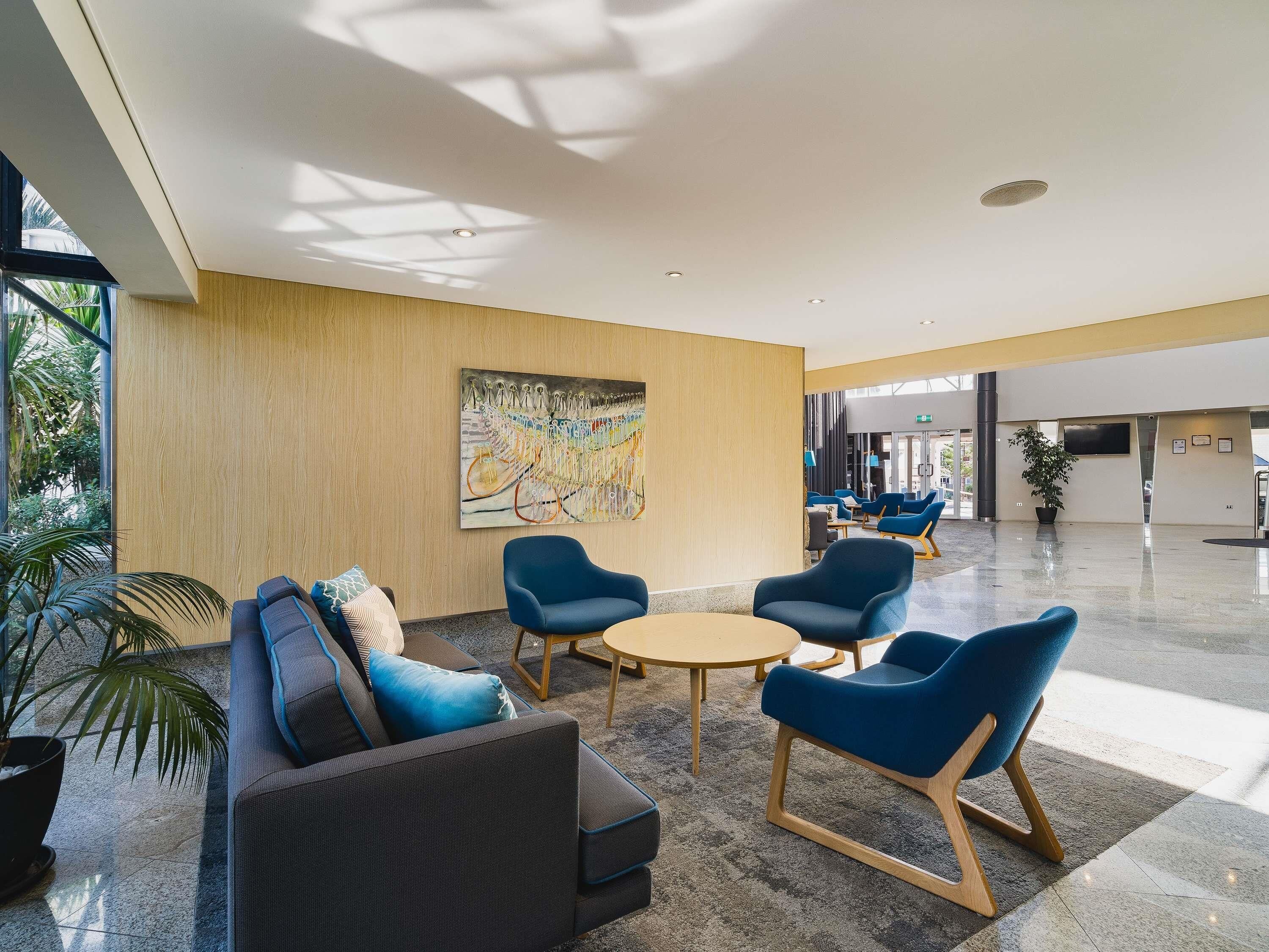 A modern lobby with a sofa, chairs, a round table, and a large abstract painting on the wall.
