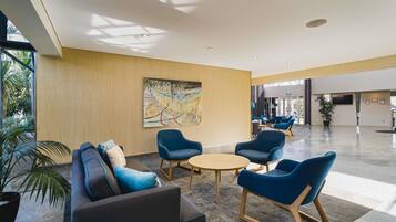 A modern lobby with a sofa, chairs, a round table, and a large abstract painting on the wall.