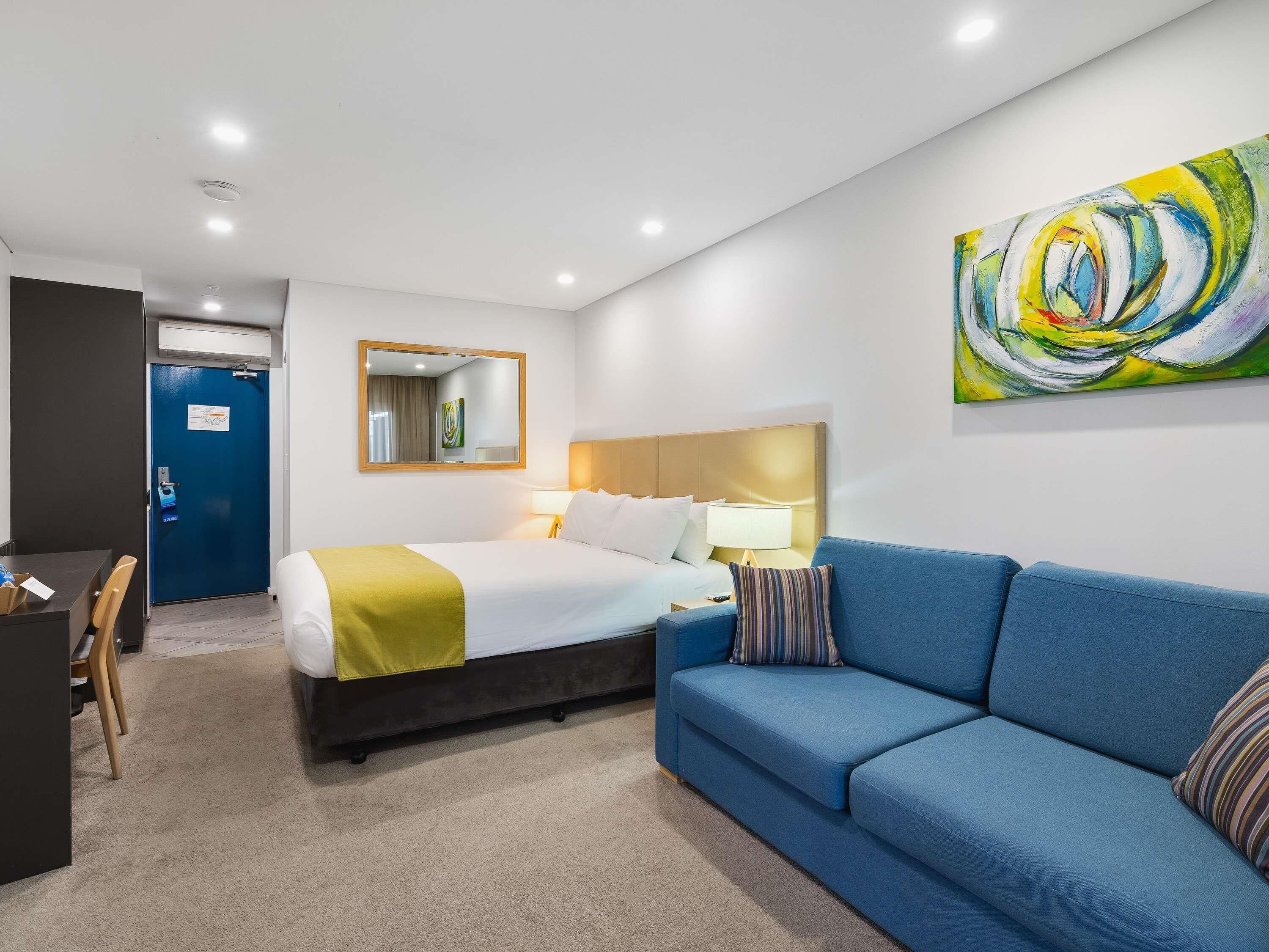 Una habitación de hotel con una cama, un sofá azul, un escritorio y un cuadro en la pared.