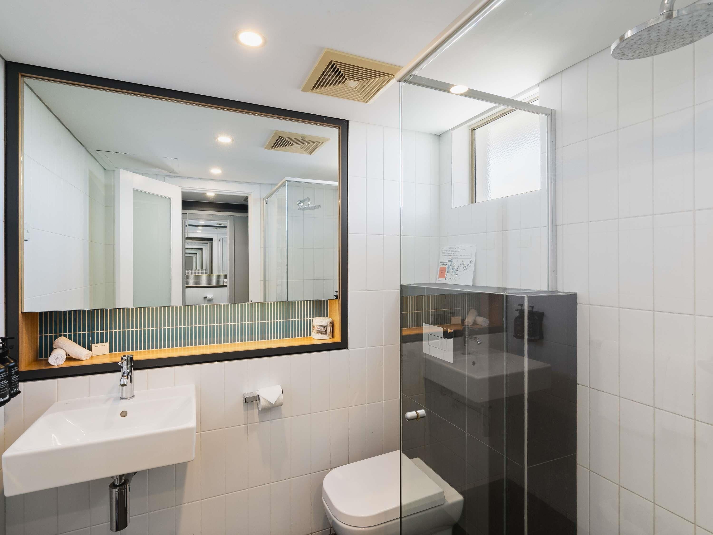 A modern bathroom with a large mirror, a sink, a toilet, and a shower.