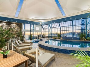 Un área de piscina con sillones reclinables, un muro de piedra y ventanas amplias.