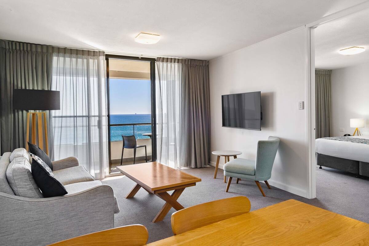 Una camera d'hotel con balcone, divano, tavolo, sedia, televisore e letto.