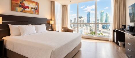 A hotel room with a large bed, a city view, a desk, and a television.