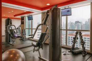 Un gimnasio con equipo de ejercicio, televisión y vista a la ciudad.