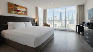 Habitación de hotel con una cama grande, un escritorio, una silla, un cuadro y vistas a la ciudad.