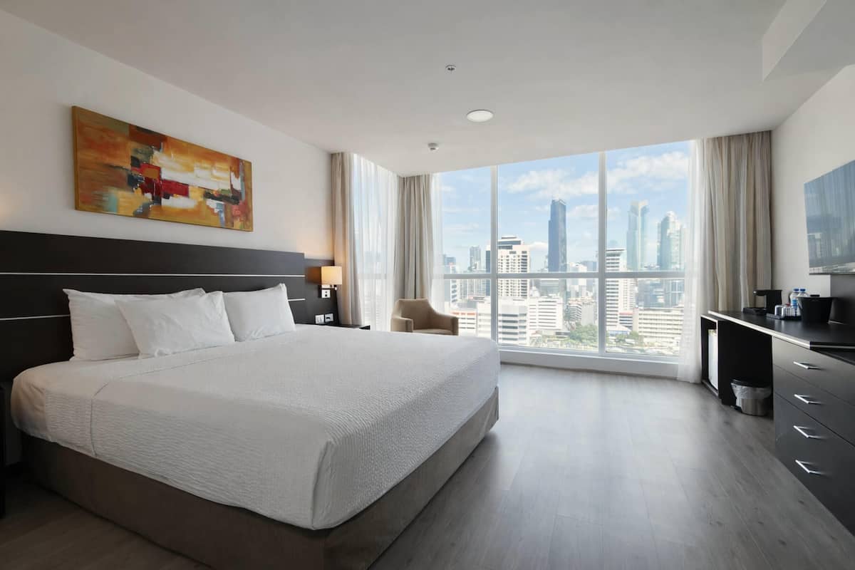 Habitación de hotel con una cama grande, un escritorio, una silla, un cuadro y vistas a la ciudad.