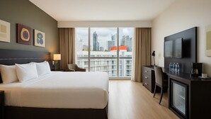 Habitación de hotel con una cama grande, un escritorio con televisor y vistas a la ciudad.