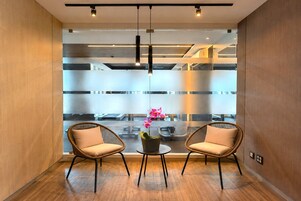 Un interior moderno con dos sillones de mimbre, una mesita con una orquídea en maceta y vistas a través de un panel de vidrio esmerilado.