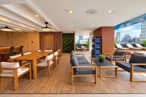 Un hall d’hôtel moderne avec un comptoir d’accueil en bois, un espace salon et une vue sur le paysage urbain.