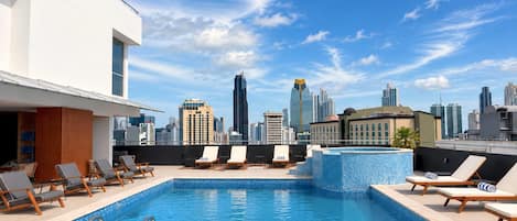 A rooftop pool with lounge chairs and a city skyline view.