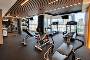 Un gimnasio moderno con diverso equipo de ejercicio, amplias ventanas con vistas a la ciudad e iluminación lineal en el techo.