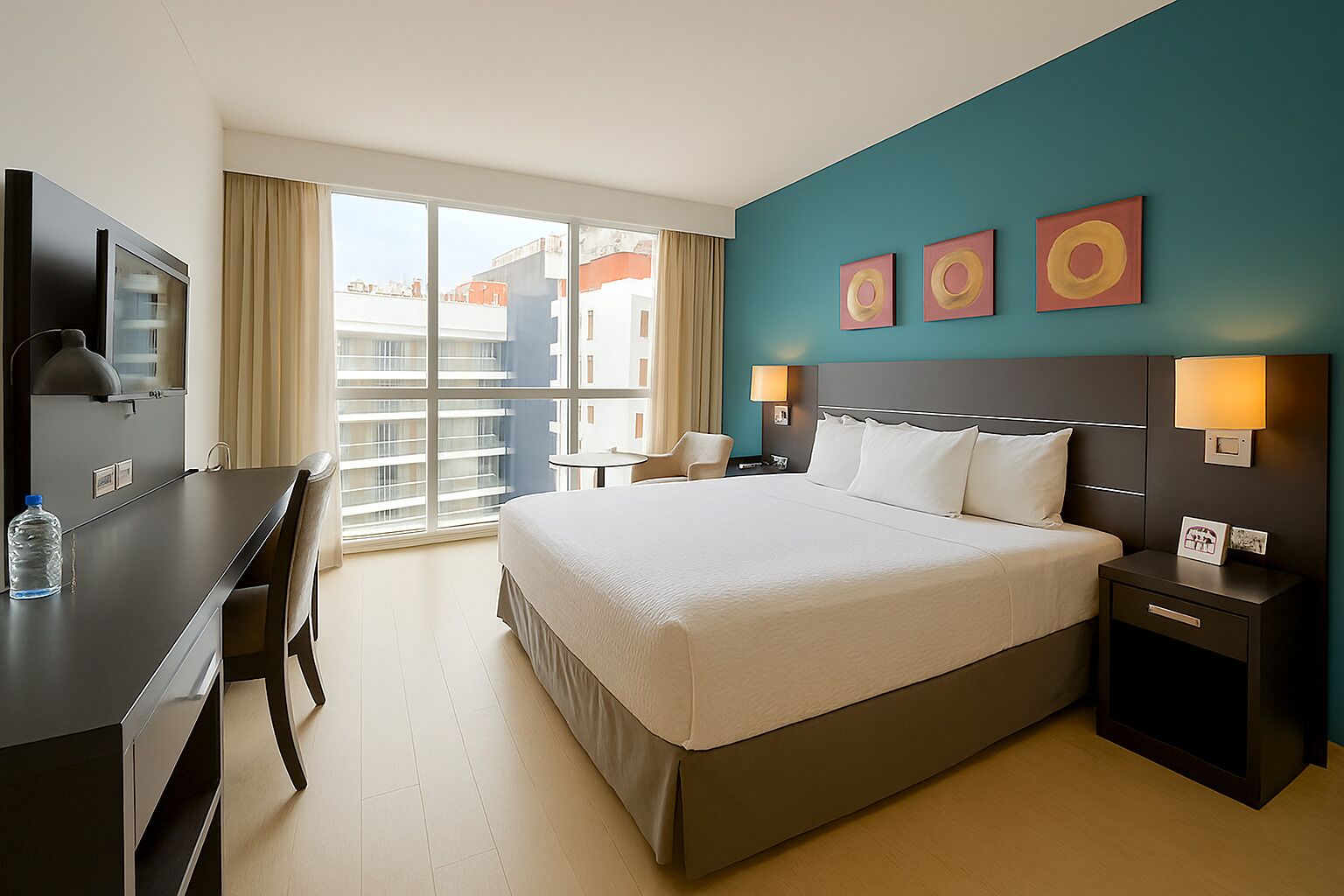 Habitación de hotel con una cama grande, un escritorio, una silla, un televisor y una ventana con vistas a la ciudad.