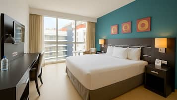 Habitación de hotel con una cama grande, un escritorio, una silla, un televisor y una ventana con vistas a la ciudad.
