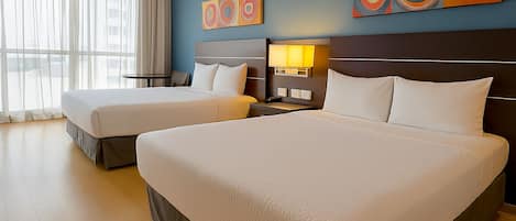 A hotel room with two beds, a large window with curtains, and abstract wall art.