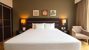 Une chambre d’hôtel avec un grand lit, deux tables de chevet avec des lampes, une chaise et des œuvres d’art accrochées au mur.